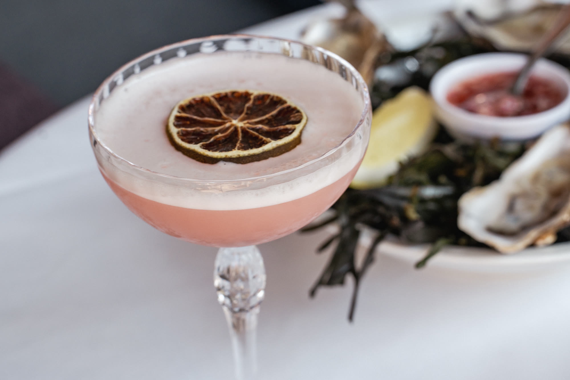 Roze cocktail met een schijfje gedroogde citrus naast een schaal oesters bij La Nostra Gigi in Amsterdam